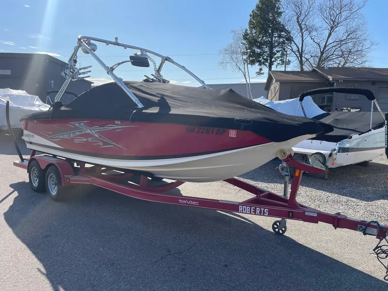 Slide: The Image of 2010 MasterCraft X-25 boat on a red trailer, covered and parked outdoors. - 2