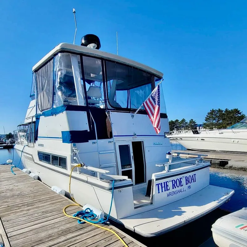 Slide: The Image of 1994 Carver 390CPMY yacht docked, displaying an American flag, named "The Roe Boat." - 2