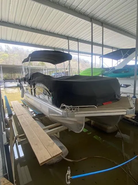 Slide: The Image of 2018 JC TriToon boat docked under a covered marina, featuring a black cover. - 1