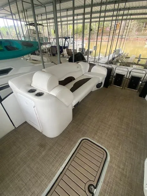 Slide: The Image of 2018 JC TriToon boat with white seating, docked under a covered marina. - 12