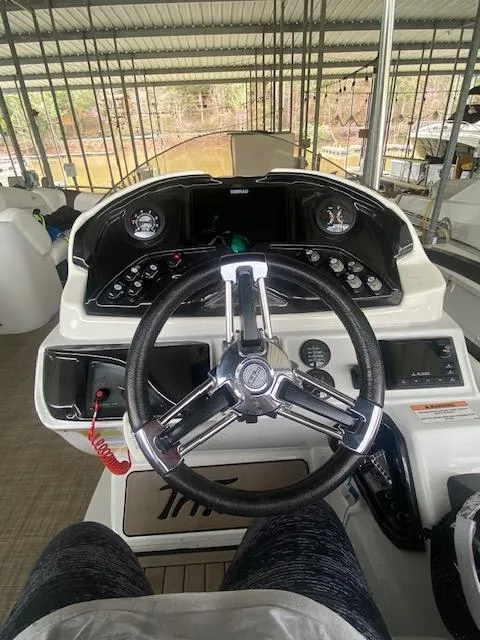 Slide: The Image of 2018 JC TriToon boat dashboard with steering wheel and control panel in a covered dock. - 7