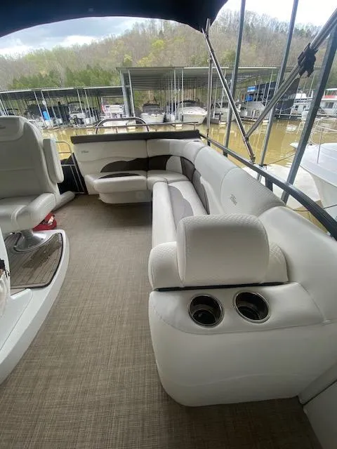 Slide: The Image of 2018 JC TriToon boat interior with plush seating and cup holders, docked at a marina. - 9