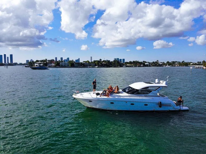 The Image of 2000 Carver 440 Hardtop Express yacht cruising on a sunny day with city skyline backdrop. - 1
