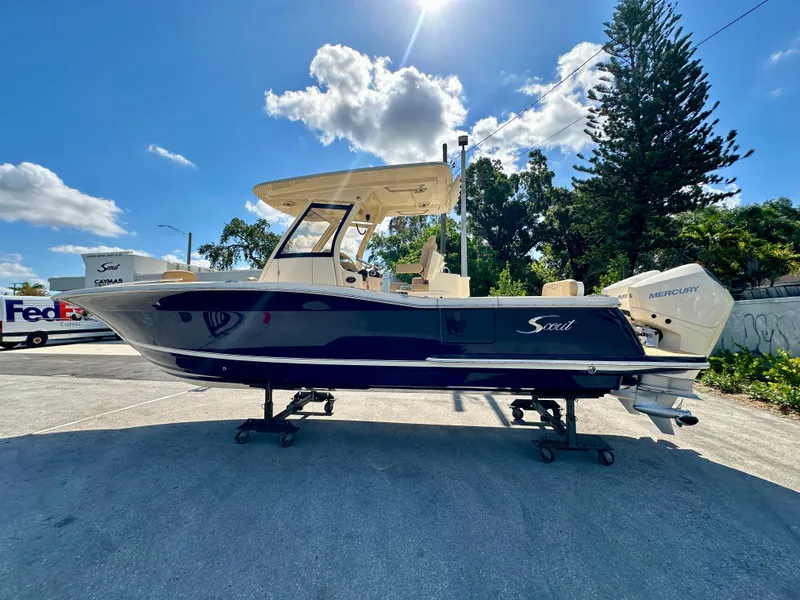 Slide: The Image of 2025 Scout 277 LXF boat with Mercury engine, parked outdoors under a sunny sky. - 2