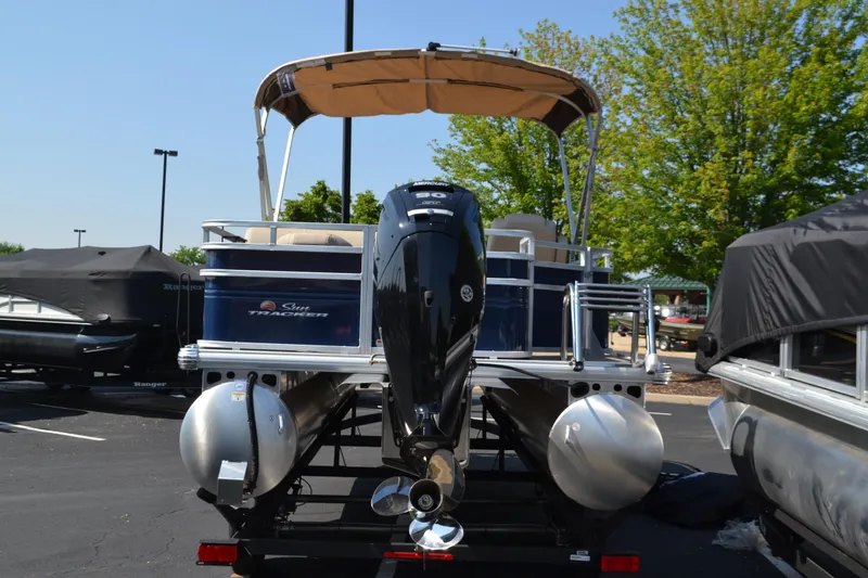 Slide: The Image of 2025 Sun Tracker Fishin' Barge 20 DLX pontoon boat with canopy and motor, parked outdoors. - 3