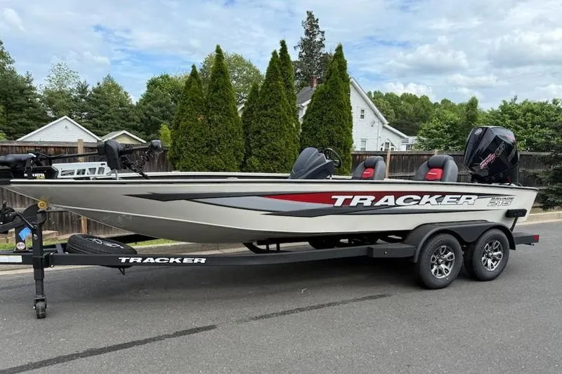 The Image of 2025 Tracker Savage 215 boat on trailer, parked on street, surrounded by trees and houses. - 0