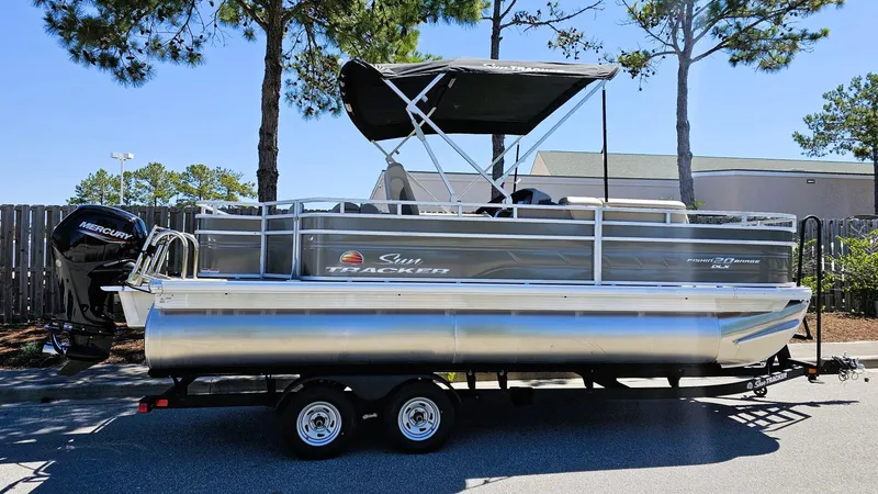 The Image of 2025 Sun Tracker Fishin' Barge 20 DLX pontoon boat on trailer, parked outdoors. - 0