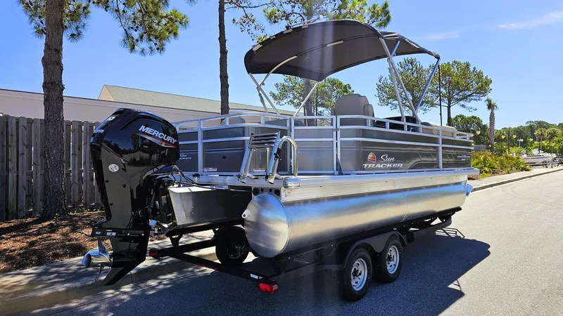 Slide: The Image of 2025 Sun Tracker Fishin' Barge 20 DLX pontoon boat on trailer, parked outdoors. - 2