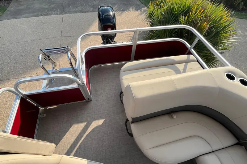 Slide: The Image of 2025 Sun Tracker Party Barge 18 DLX with beige seating and red accents, docked outdoors. - 7