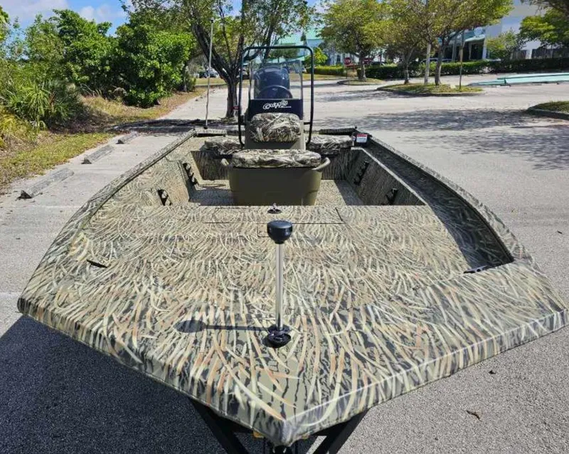 Slide: The Image of 2025 Tracker Grizzly 1860 CC boat with camouflage design, parked outdoors. - 2