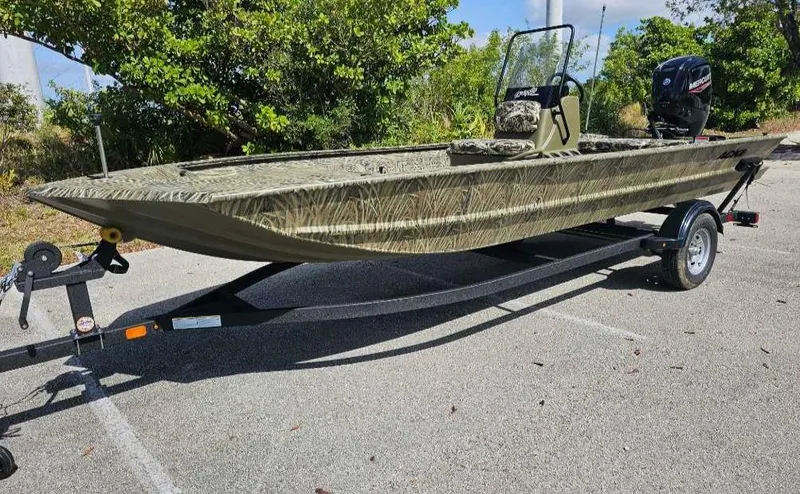 Slide: The Image of 2025 Tracker Grizzly 1860 CC boat on trailer, parked outdoors, surrounded by greenery. - 3