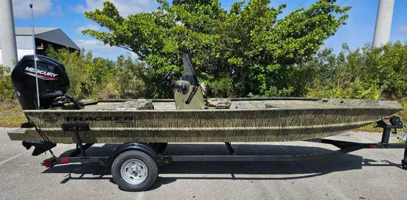 Slide: The Image of 2025 Tracker Grizzly 1860 CC boat on trailer, parked outdoors with trees in background. - 71