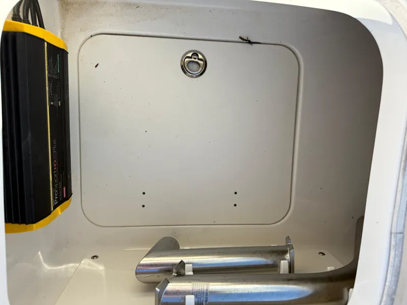Slide: The Image of 2021 Robalo 246 Cayman storage compartment with battery charger and metal components. - 17