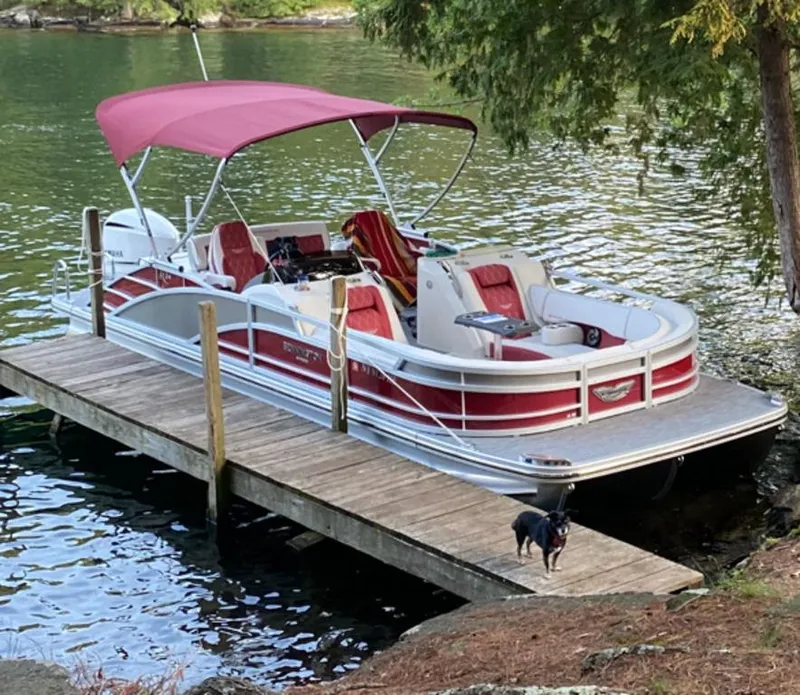 Slide: The Image of 2021 Bennington 24 RTSB pontoon boat docked on a serene lake with a red canopy. - 1