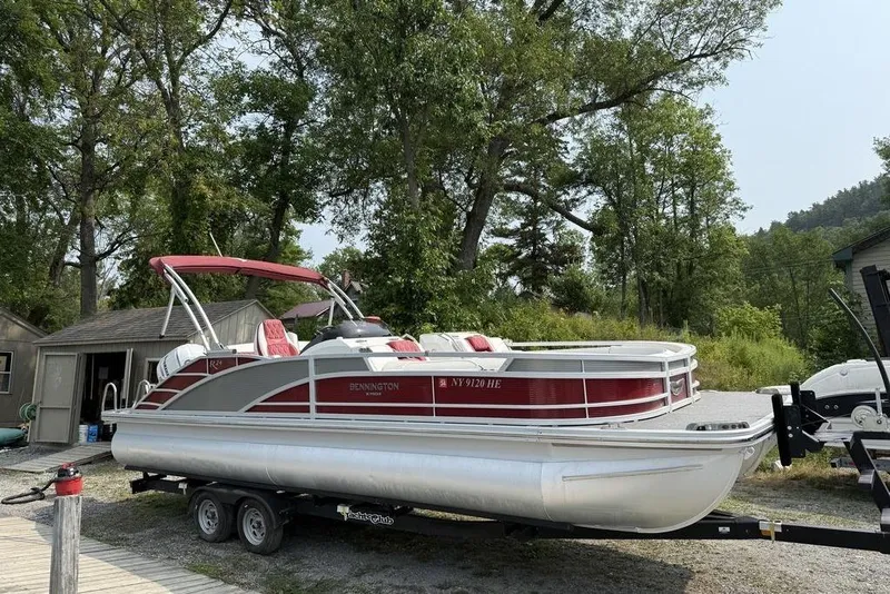 Slide: The Image of 2021 Bennington 24 RTSB pontoon boat on trailer, surrounded by trees and a small building. - 3
