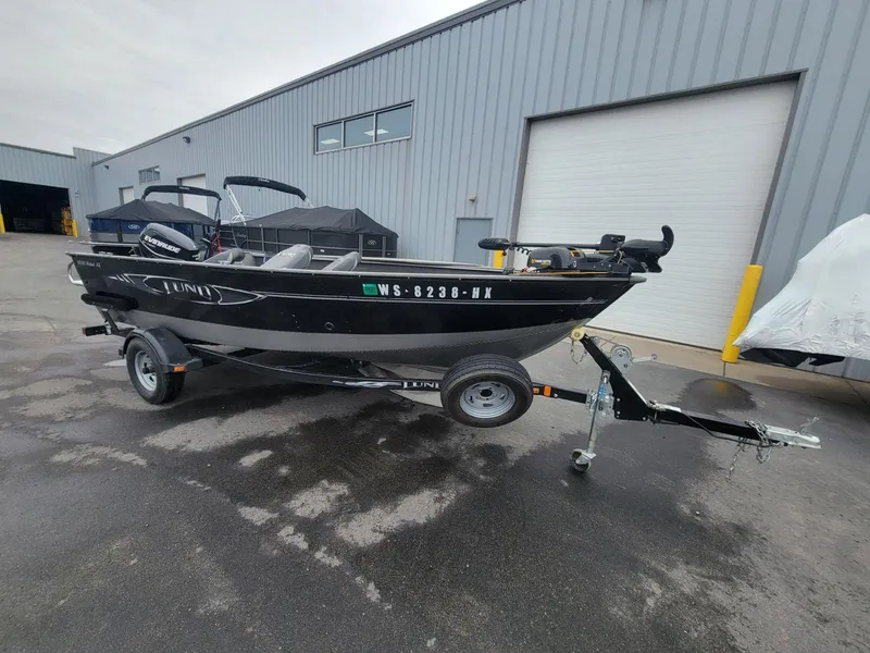 Slide: The Image of 2013 Lund 1650 Rebel XL Tiller boat on trailer, parked outside industrial building. - 11