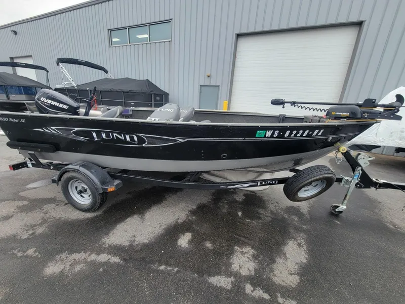 Slide: The Image of 2013 Lund 1650 Rebel XL Tiller boat on trailer, parked outside industrial building. - 12