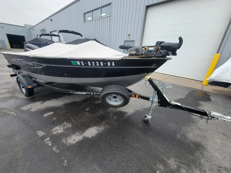 Slide: The Image of 2013 Lund 1650 Rebel XL Tiller boat on trailer, covered, parked outside a warehouse. - 7