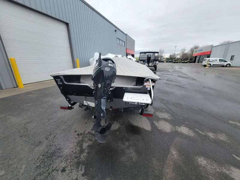 Slide: The Image of 2013 Lund 1650 Rebel XL Tiller boat with outboard motor, parked outside a warehouse. - 9