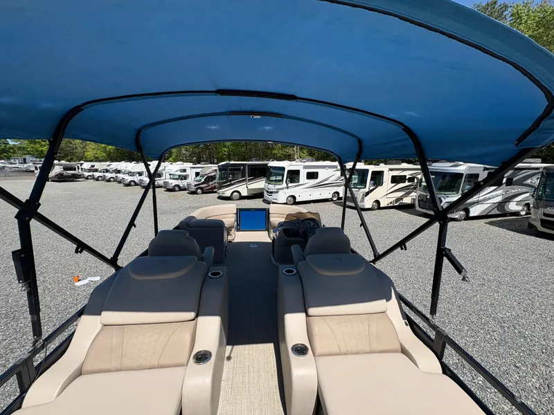 Slide: The Image of 2018 Avalon LSZ Quad Lounger boat with blue canopy, parked near RVs. - 15