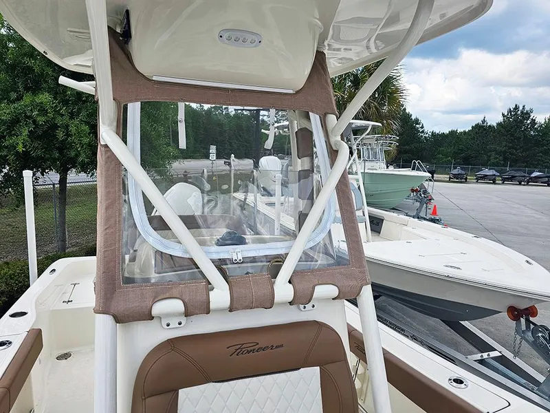 Slide: The Image of 2025 Pioneer 220 Bay Sport boat with tan seating and clear windshield, parked outdoors. - 20