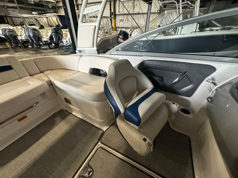 Slide: The Image of 2018 Chaparral 244 Sunesta boat interior with beige and blue seating in a showroom. - 33