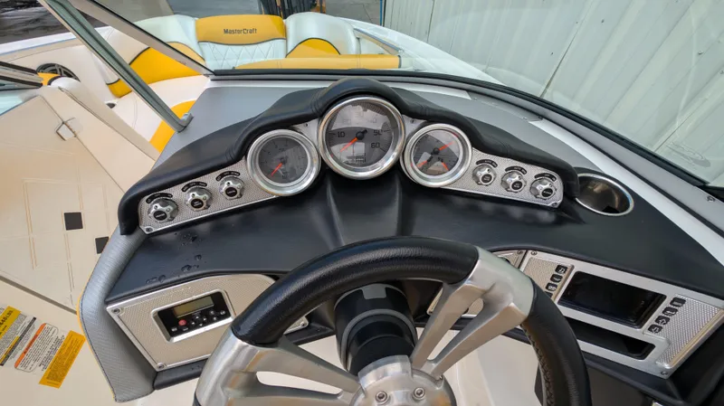 Slide: The Image of 2013 MasterCraft X2 boat dashboard with gauges and steering wheel, featuring yellow seating. - 14