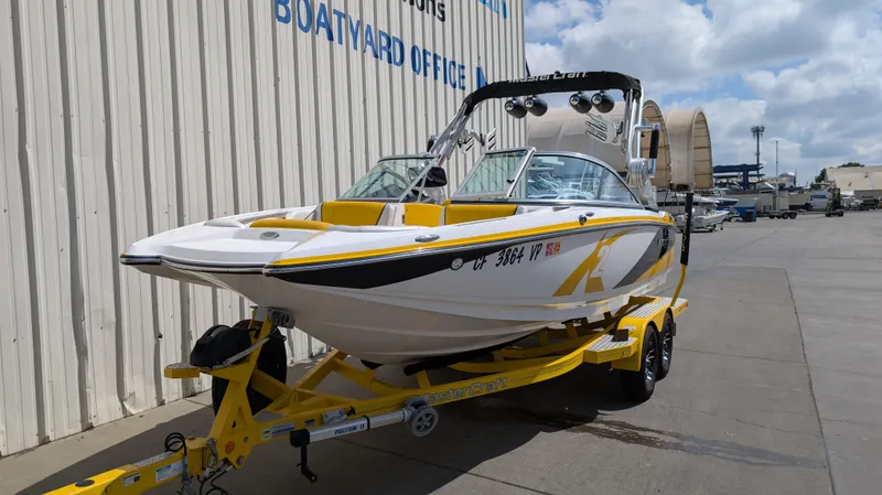 Slide: The Image of 2013 MasterCraft X2 boat on yellow trailer, parked near a boatyard office. - 2