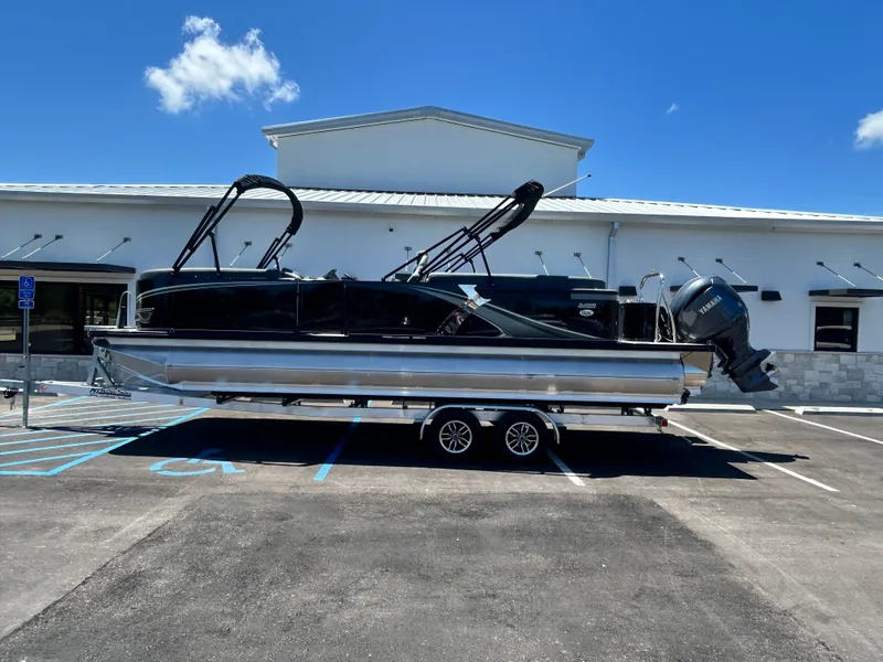 Slide: The Image of 2025 Tahoe LTZ QL25T pontoon boat on trailer, parked in front of a building. - 1