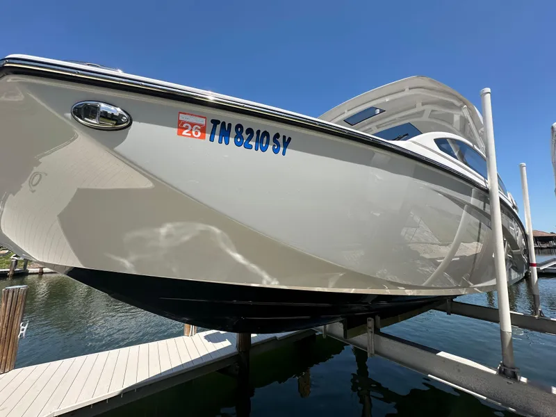 Slide: The Image of 2023 Yamaha Boats 275 SDX on lift, docked at marina under clear blue sky. - 13