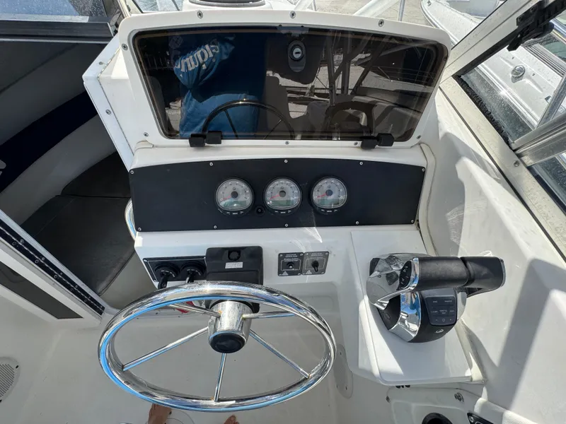 Slide: The Image of 1999 Boston Whaler Conquest 23 helm with steering wheel, gauges, and throttle controls. - 16