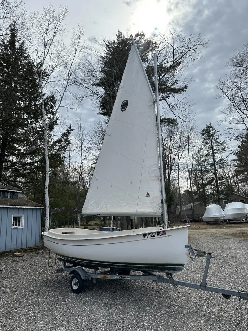 Slide: The Image of 2001 Com-Pac Picnic Cat sailboat on trailer, surrounded by trees and overcast sky. - 1