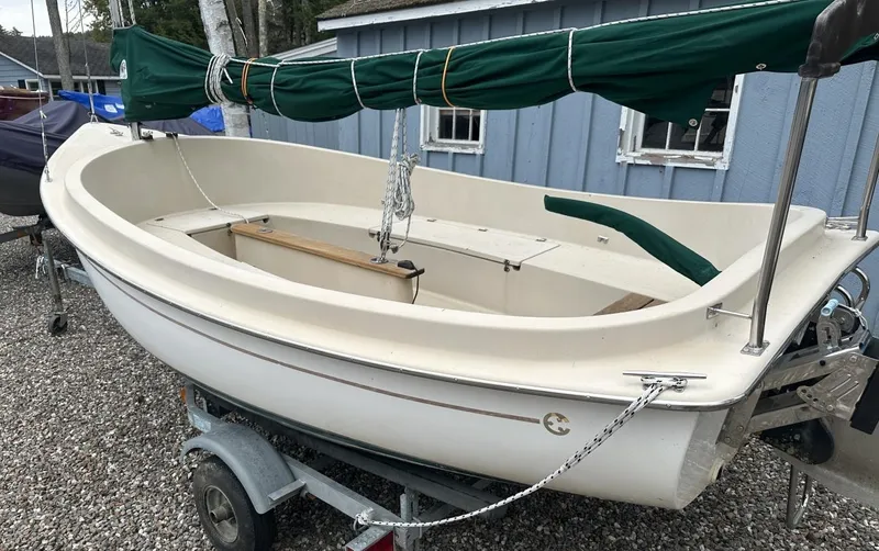 Slide: The Image of 2001 Com-Pac Picnic Cat sailboat on trailer, green sail cover, parked on gravel. - 3