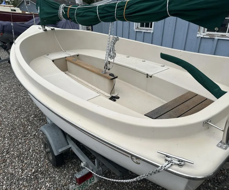 Slide: The Image of 2001 Com-Pac Picnic Cat sailboat on trailer, featuring green sail cover and wooden seating. - 5