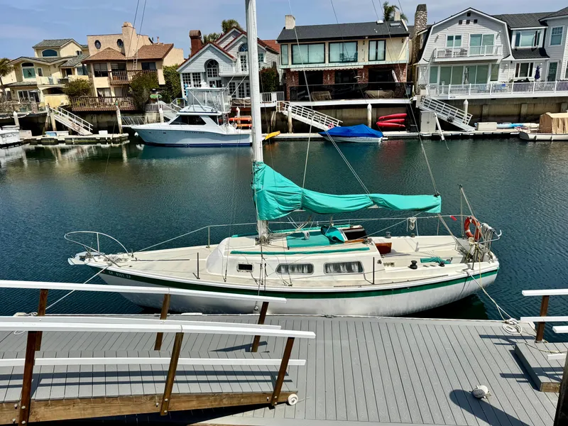 The Image of 1970 CAL 29 sailboat docked in a scenic marina with waterfront homes. - 0