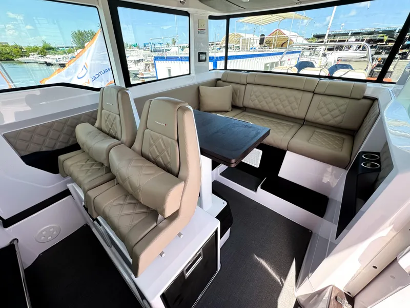 Slide: The Image of 2023 Axopar 37 XC CROSS CABIN interior with beige seating and table, docked at marina. - 10