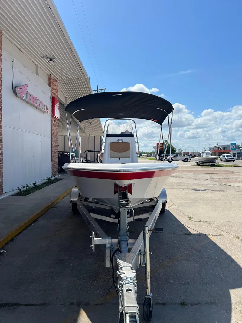 Slide: The Image of 2025 NauticStar 194 Bay boat on trailer, parked outside dealership under clear blue sky. - 4