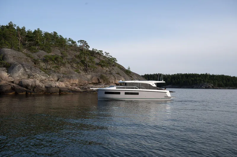 Slide: The Image of 2025 Delphia D11 SEDAN yacht cruising near rocky shoreline and forested landscape. - 3