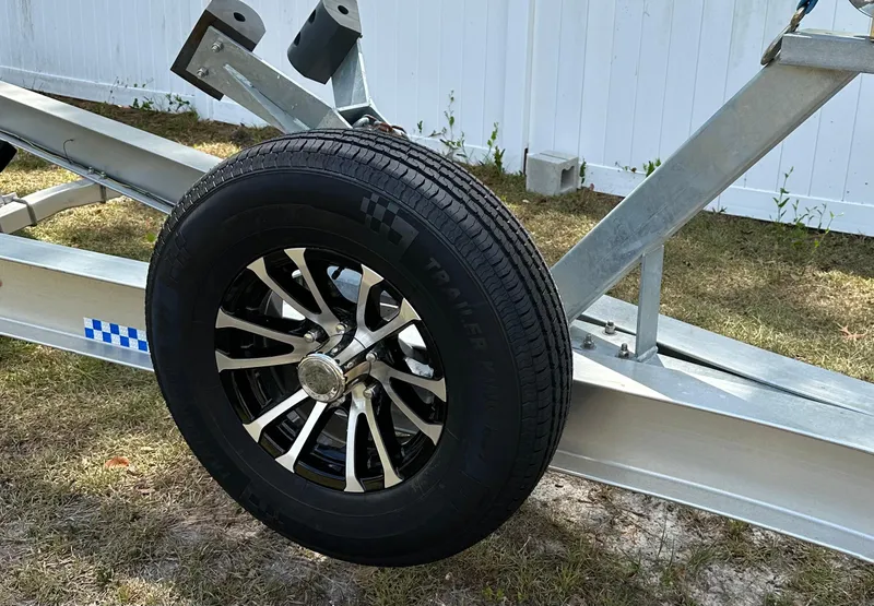 Slide: The Image of Trailer wheel on grass, part of a 2018 Sailfish 325 DC boat trailer. - 18
