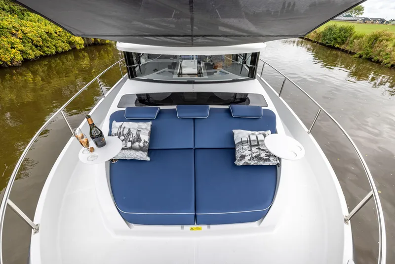 Slide: The Image of 2025 Delphia D11 Flybridge yacht with blue sunbed, pillows, and drinks on a river. - 9