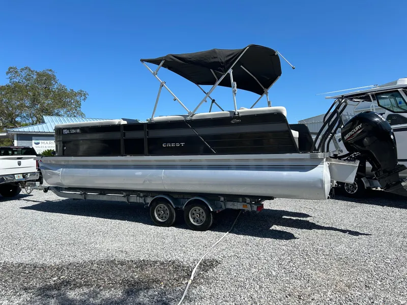 Slide: The Image of 2021 Crest 240 LX SLSC pontoon boat on trailer, black canopy, parked outdoors. - 2