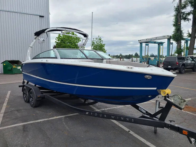 Slide: The Image of 2023 Four Winns H4 boat in blue on a trailer, parked outdoors. - 3