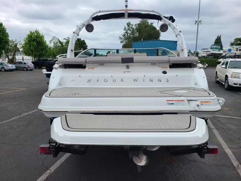 Slide: The Image of 2023 Four Winns H4 boat rear view in parking lot, showcasing swim platform and seating. - 5