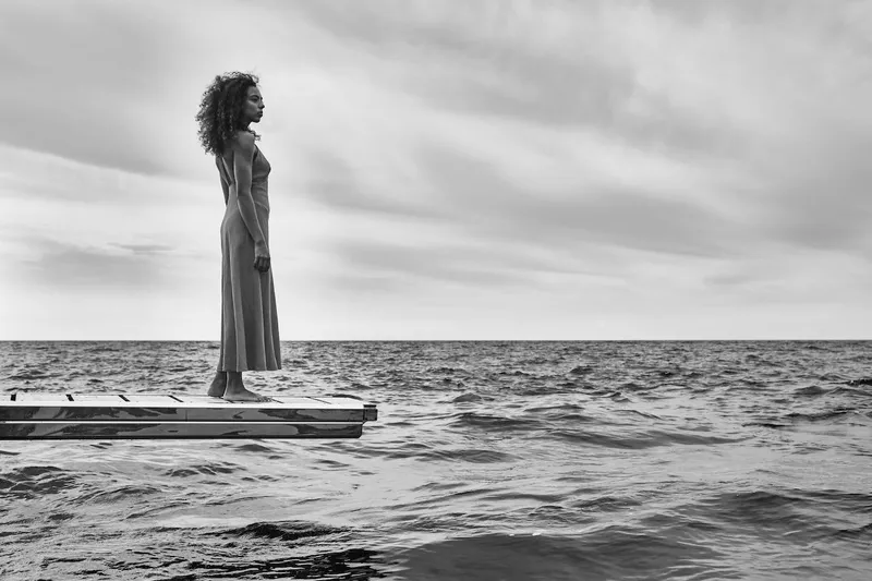 Slide: The Image of A woman stands on a dock, gazing at the ocean under a cloudy sky. - 78