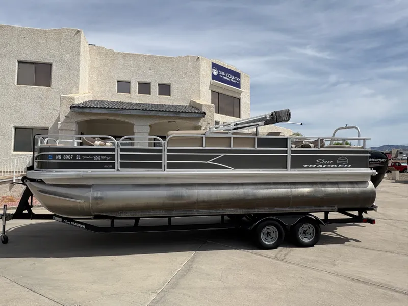 Slide: The Image of 2017 Sun Tracker Fishin' Barge 22 DLX pontoon boat on trailer, parked outside building. - 3