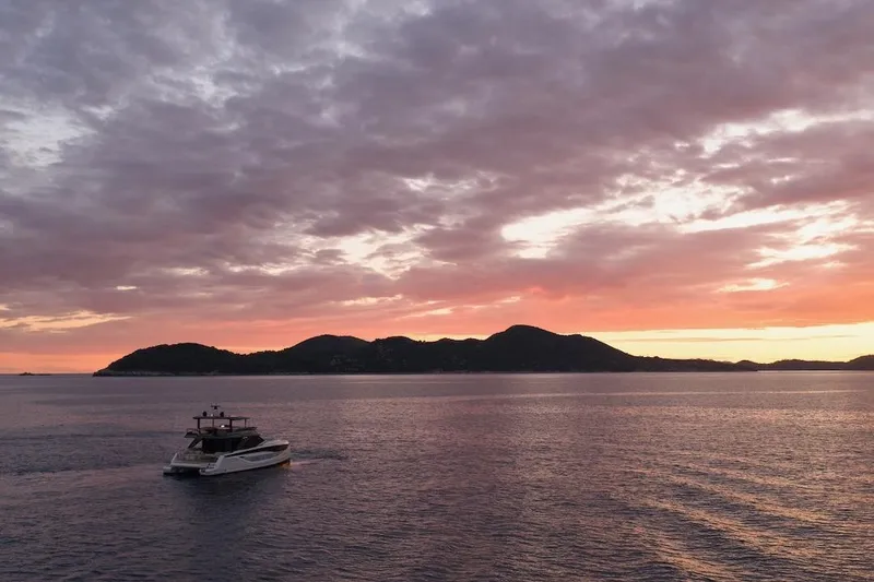 Slide: The Image of Sunset over ocean with Prestige M7 yacht, 2025 model, near silhouetted islands. - 112