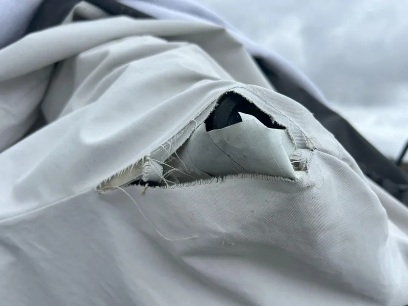 Slide: The Image of Torn cover on 2015 Sea-Doo GTX 155, revealing underlying material, against cloudy sky. - 28