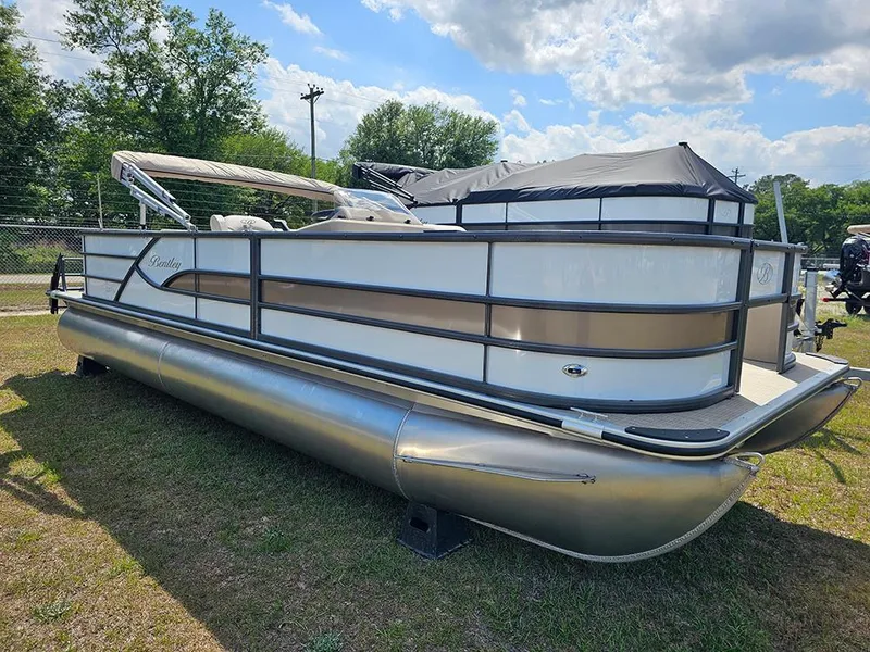 Slide: The Image of 2025 Bentley Pontoons 240 4-Point Fish pontoon boat on grass under a partly cloudy sky. - 2