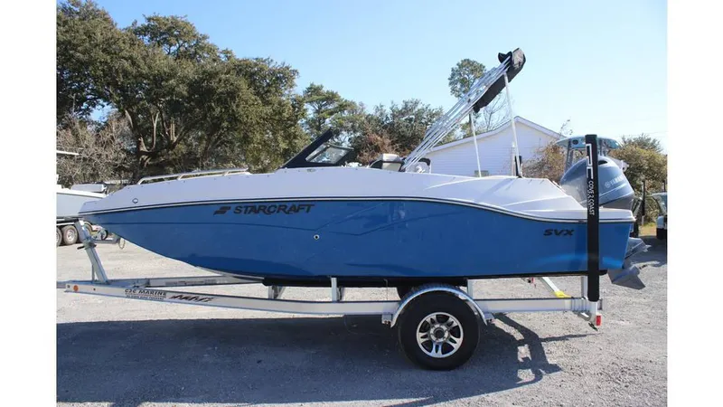 Slide: The Image of 2025 Starcraft SVX 190 OB DC boat on trailer, blue and white design, parked outdoors. - 5