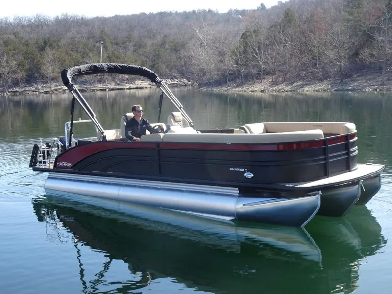 Slide: The Image of 2025 Harris Sunliner 250 pontoon boat on a calm lake with scenic background. - 0